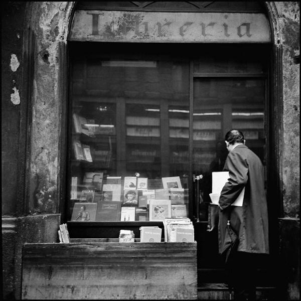 Milano - Via Cusani 7 - Libreria, esterno - Uomo all'entrata con ombrello e documenti in mano - Vetrina con libri in esposizione - Libri esposti all'esterno in una cassa di legno - Insegna