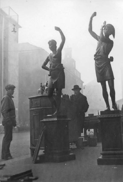 Milano panorami: Milano centro. Milano - Statue di bronzo: mori - Merce esposta su strada - Due uomini - Rigattiere - Nebbia - Palazzi