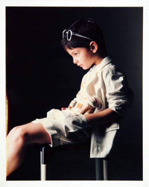 Campagna pubblicitaria per Trussardi Junior - Bambino seduto di profilo: pantaloncini e maglietta bianchi, occhiali da sole