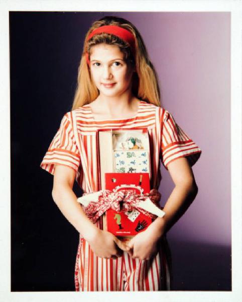 Campagna pubblicitaria per Trussardi Junior - Bambina con abito a righe bianche e rosse - Cerchietto rosso - Scatola con giochi tra le braccia