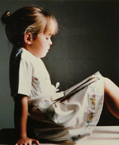 Campagna pubblicitaria per Trussardi Junior - Bambina seduta di profilo: maglioncino bianco ricamato e gonna con animali sull'orlo - Libro