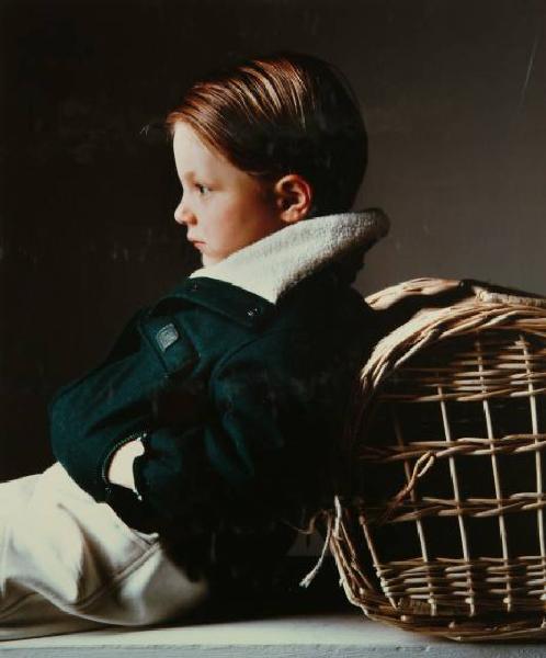 Campagna pubblicitaria per Trussardi Junior - Bambino seduto di profilo: giubbotto verde scuro su pantaloni bianchi