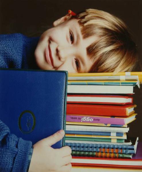 Campagna pubblicitaria per Trussardi Junior - Bambino sorridente: maglione blu - Appoggia il capo su una pila di quaderni