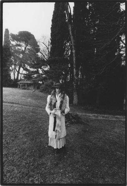 Giovane donna posa in un giardino indossando un cappotto con stola di volpe e cappello con veletta