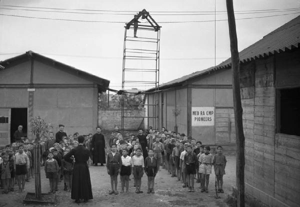 Italia del Sud. Puglia - Bari - Villaggio dei Fanciulli - bambini in fila tra le baracche - prete