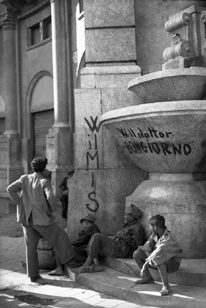 Italia del Sud. Sicilia - Palermo - ragazzi seduti ai piedi di una fontana - sulla vasca la scritta W IL DOTTOR BONGIORNO