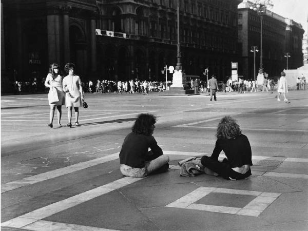 Mondo Beat. Milano - Piazza del Duomo - Due ragazzi seduti in mezzo alla piazza - Passanti