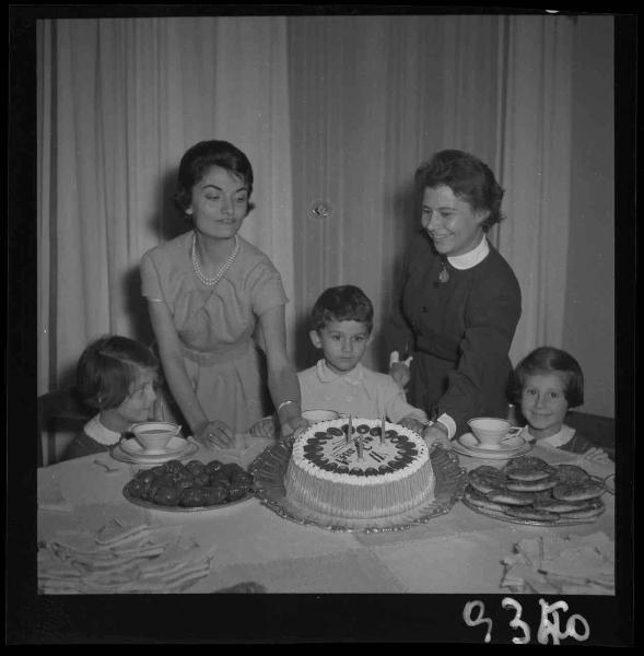 Ritratto di gruppo - Famiglia Morenghi - Bambino davanti alla torta con candeline - Due adulte nell'atto di mostrare la torta - Bambine a tavola