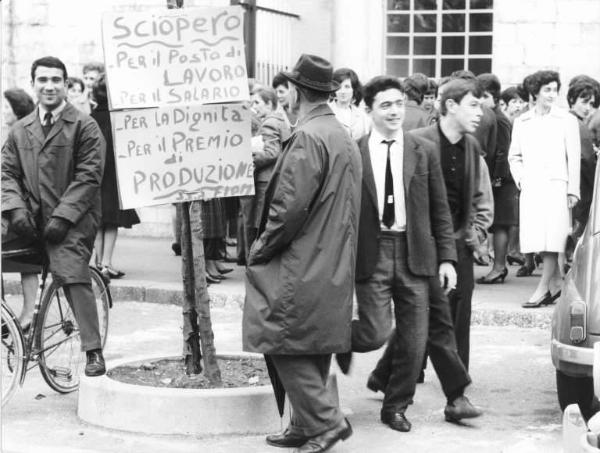 Sciopero dei lavoratori della Sit Siemens contro la riduzione dell'orario di lavoro - Uomo legge cartello di sciopero della Fiom - Donne davanti alla fabbrica