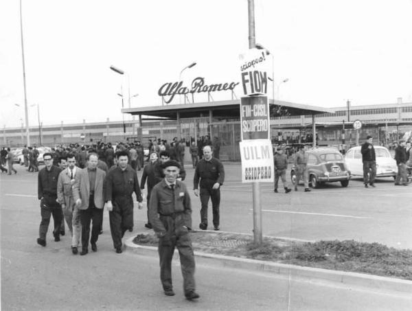 Sciopero dei lavoratori dell'Alfa Romeo di Arese - Lavoratori davanti all'ingresso della fabbrica - Operai con tuta da lavoro - Cartelli Fiom, Fim Cisl, Uilm - Insegna Alfa Romeo