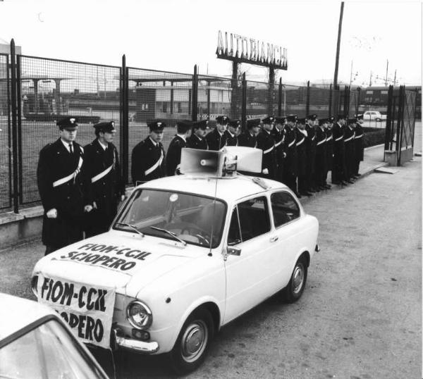 Sciopero dei lavoratori della Autobianchi - Schieramento delle forze dell'ordine davanti all'ingresso della fabbrica - Auto con altoparlante e striscione Fiom Cgil - Insegna Autobianchi