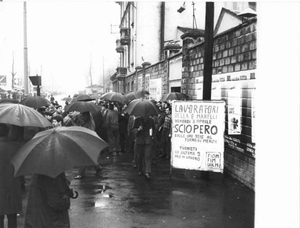 Sciopero dei lavoratori della Ercole Marelli - Ingresso della fabbrica - Presidio sotto la pioggia - Operai con tuta da lavoro - Cartello di sciopero Fiom, Fim, Uilm