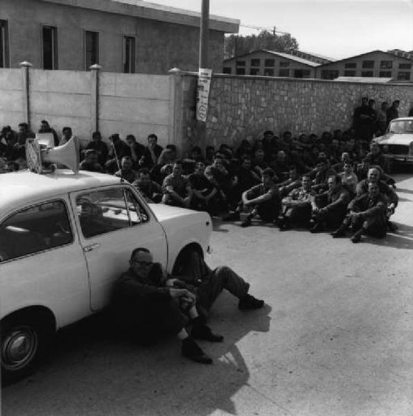 Sciopero dei lavoratori della Tlm per la riduzione dell'orario di lavoro - Lavoratori seduti davanti alla fabbrica - Operai con tuta da lavoro - Auto con altoparlante