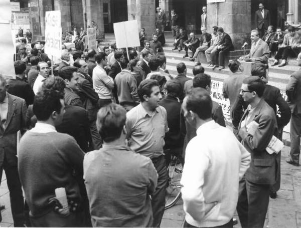 Sciopero dei lavoratori edili contro gli omicidi bianchi e gli infortuni - Piazza Mercanti - Comizio - Oratore al microfono - Cartelli di rivendicazione