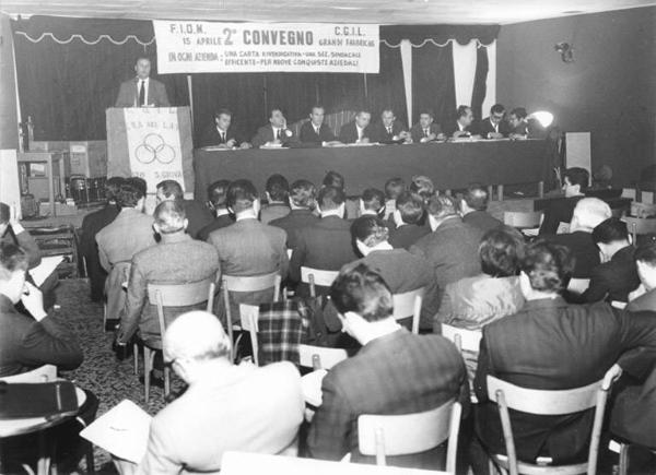 Camera del Lavoro di Sesto San Giovanni - Interno - Secondo convegno delle grandi fabbriche organizzato dalla Fiom Cgil - Palco - Tavolo della presidenza - Annio Breschi al microfono - Platea di spalle - Parola d'ordine del convegno