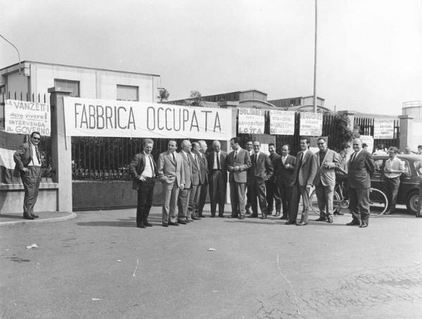 Occupazione alla Vanzetti contro i licenziamenti - Foto di gruppo dei parlamentari davanti al cancello di ingresso della fabbrica - Striscione "fabbrica occupata" e cartelli di protesta