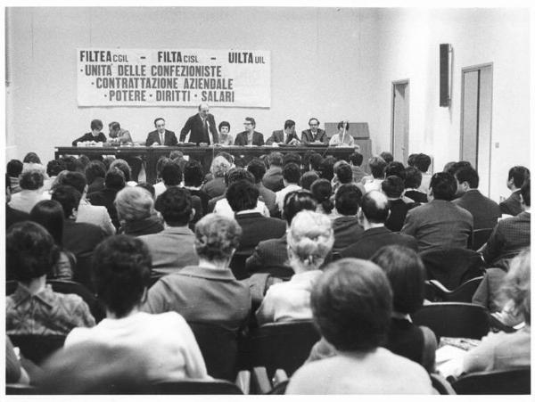 Convegno unitario dei lavoratori delle confezioni - Interno - Panoramica sulla sala - Tavolo della presidenza - Parola d'ordine - Platea con pubblico di spalle