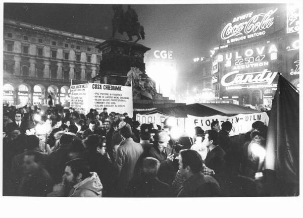 Piazza del Duomo - Notte di Capodanno - Presidio dei lavoratori della Borletti e di altre fabbriche in lotta - Tenda - Lavoratori - Cartelli di rivendicazione - Striscioni - Monumento a Vittorio Emanuele II - Pubblicità sui palazzi