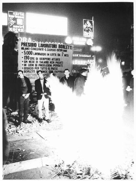 Piazza del Duomo - Notte di Capodanno - Presidio dei lavoratori della Borletti e di altre fabbriche in lotta - Lavoratori davanti al fuoco - Cartelli di rivendicazioni - Pubblicità sui palazzi