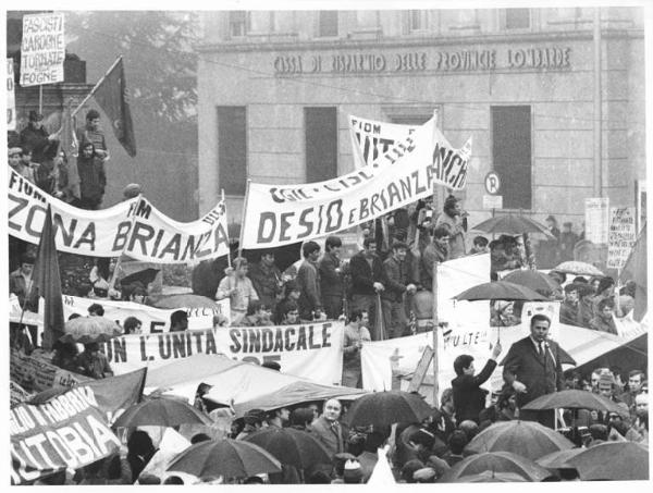 Sciopero generale in solidarietà con i lavoratori dell'Autobianchi - Piazza Conciliazione - Comizio sotto la pioggia - Roberto Romei al microfono - Operai con tuta da lavoro - Striscioni - Bandiere