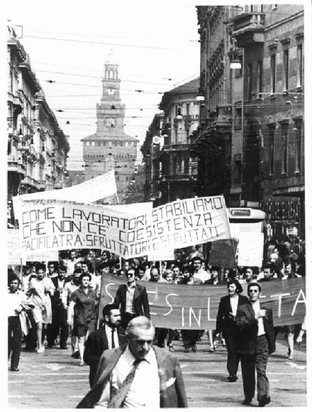 Sciopero unitario lavoratori della zona Sempione - Corteo in via Dante - Spezzone lavoratori della Saes - Operaie con grembiule da lavoro - Striscioni - Cartelli - Sullo sfondo il Castello Sforzesco