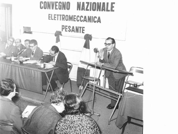 Casa della cultura - Interno - Convegno nazionale elettromeccanica pesante - Palco - Oratore al microfono - Al tavolo della presidenza Piero Boni e Bruno Trentin - Parola d'ordine del convegno