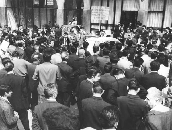 Sciopero unitario dei lavoratori edili - Comizio in piazza Santo Stefano - Oratore al microfono - Lavoratori - Cartello di protesta - Auto con altoparlanti