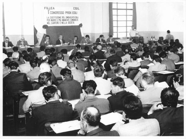 Camera del Lavoro - Sala "Bruno Buozzi" - Interno - Congresso provinciale edili - Panoramica sulla sala - Tavolo della presidenza - Platea con pubblico di spalle - Parola d'ordine del congresso