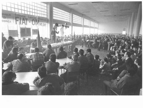 Om Fiat - Interno - Assemblea permanente dei lavoratori per il contratto - Panoramica sulla sala - Oratore al microfono - Operai con tuta da lavoro - Altoparlante - Striscione - Bandiere