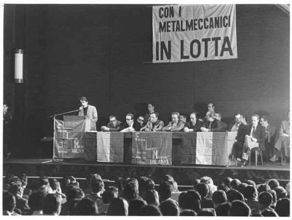 Teatro Lirico - Interno - Assemblea dei parlamentari eletti con i consigli di fabbrica metalmeccanici - Tavolo della presidenza con tra gli altri A. Breschi, R. Romei, G. Cervetti, L. Banfi - Delegato di fabbrica al microfono - Parola d'ordine