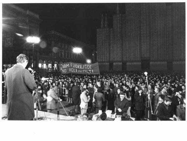 Presidio dei lavoratori metalmeccanici in piazza del Duomo tutta la giornata - Comizio serale conclusivo - Palco - Lucio De Carlini di spalle al microfono - Folla di lavoratori - Striscione Ibm - Il Duomo con impalcature