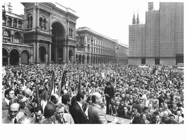 Manifestazione del primo maggio - Comizio in piazza del Duomo - Panoramica della piazza - Sul palco Piero Boni al microfono, al suo fianco L. De Carlini e R. Romei - Folla di lavoratori - Bandiere - Il Duomo con impalcature