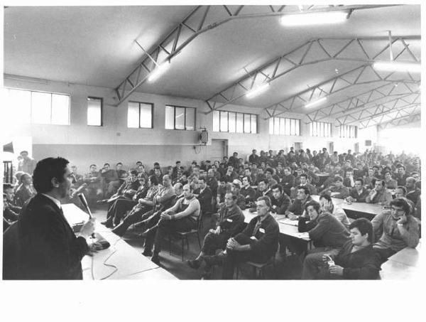 Falck - Interno - Assemblea congressuale in fabbrica - Lucio De Carlini al microfono - Panoramica sulla platea - Operai con tuta da lavoro