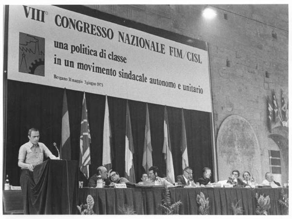 Sala - Interno - VIII congresso nazionale della Fim Cisl - Tavolo della presidenza - Pierre Carniti al microfono - Parola d'ordine - Bandiere