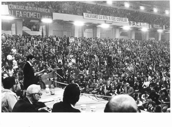 Palazzetto dello sport - Interno - Manifestazione per il Cile - Tavolo della presidenza - Mario Colombo al microfono - Platea con manifestanti - Striscioni - Bandiere