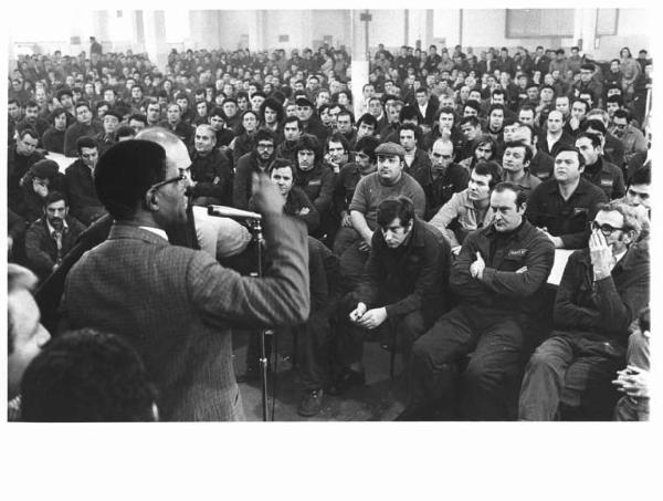 Innocenti Leyland - Interno - Assemblea dei lavoratori con il sindacalista del Sudafrica John Gaetsewe - Panoramica sulla sala - John Gaetsewe al microfono - Platea - Operai con tuta da lavoro