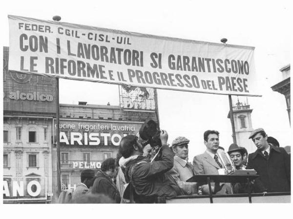 Sciopero generale per l'occupazione e le riforme - Comizio in piazza del Duomo - Palco - Luciano Lama al microfono, al suo fianco Lucio De Carlini - Parola d'ordine della manifestazione - Uomo con cinepresa - Pubblicità sui palazzi