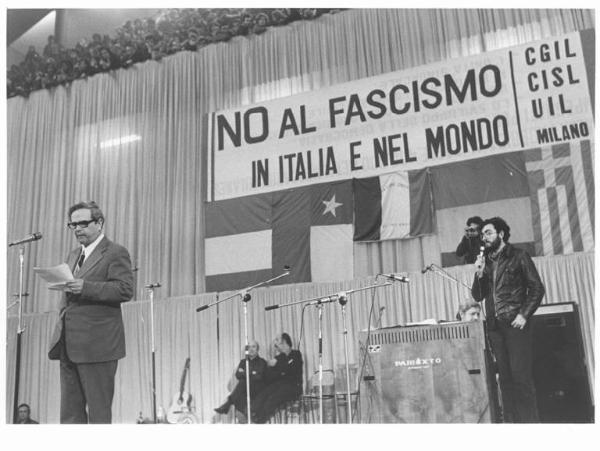 Palalido - Interno - Manifestazione antifascista e internazionalista promossa dalla Federazione Cgil, Cisl e Uil di Milano - Palco - Carlos Vallejo, sindacalista spagnolo, al microfono - Parola d'ordine della manifestazione - Bandiere