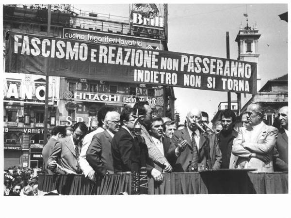 Manifestazione di tutte le categorie in risposta alla strage in piazza della Loggia a Brescia - Comizio in piazza del Duomo - Palco - Giancarlo Pajetta al microfono - Striscione - Pubblicità sui palazzi