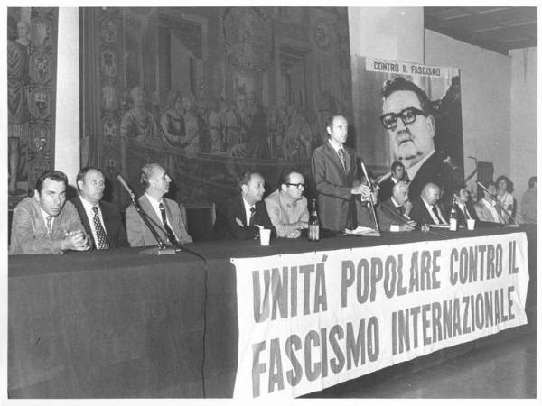 Castello Sforzesco - Sala della Balla - Interno - Manifestazione contro il fascismo internazionale a un anno dal colpo di stato in Cile - Tavolo della presidenza - Oratore al microfono - Parola d'ordine - Immagine di Salvador Allende