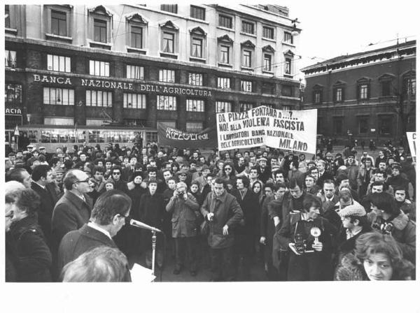 Piazza Fontana - Commemorazione dell'attentato stragista alla Banca Nazionale dell'Agricoltura - Manifestazione antifascista - Comizio - Palco - Il sindaco Aldo Aniasi al microfono - Manifestanti - Striscioni - Fotografi - Insegna della Banca