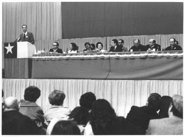 Palalido - Interno - Manifestazione in solidarietà con il Cile - Palco - Tavolo della presidenza con Lelio Basso, Hortensia Bussi de Allende, Aldo Aniasi, padre David Maria Turoldo, Luis Badilla - Lucio De Carlini al microfono - Bandiera