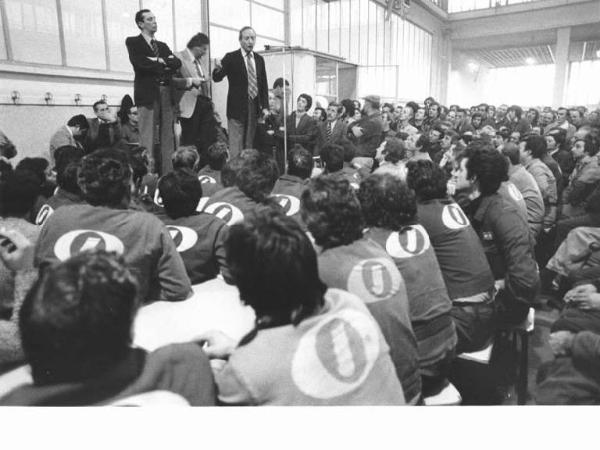 Fabbrica Innocenti Leyland (Innse) - Interno - Assemblea dei lavoratori - Palco - Bruno Storti al microfono, al suo fianco Lucio De Carlini - Platea con operai con tuta da lavoro