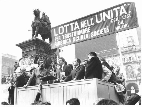 Sciopero generale dell'industria indetto dalla Federazione Cgil, Cisl, Uil - Comizio in piazza del Duomo - Palco - Giorgio Benvenuto al microfono - Parola d'ordine della manifestazione - Monumento a Vittorio Emanuele II - Striscioni - Bandiere