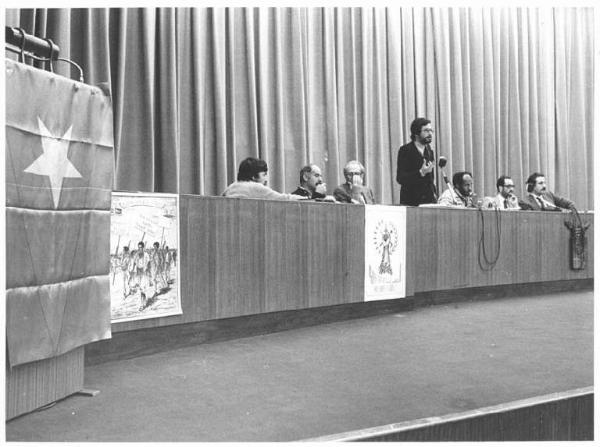 Sala dei Congressi della Provincia - Interno - Manifestazione per l'Eritrea - Tavolo della presidenza con, tra gli oratori, Sandro Antoniazzi, Leonardo Banfi, Andenichel, Bimbi, Petrucci, Torreggiani - Bandiera