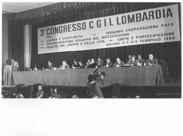 Teatro Nuovo - Interno - Terzo congresso regionale della Cgil - Tavolo della presidenza con tra gli oratori Anna Catasta, Franco Torri, Antonio Pizzinato, Jone Bagnoli, Annio Breschi - Alberto Bellocchio al microfono - Parola d'ordine - Cineoperatore