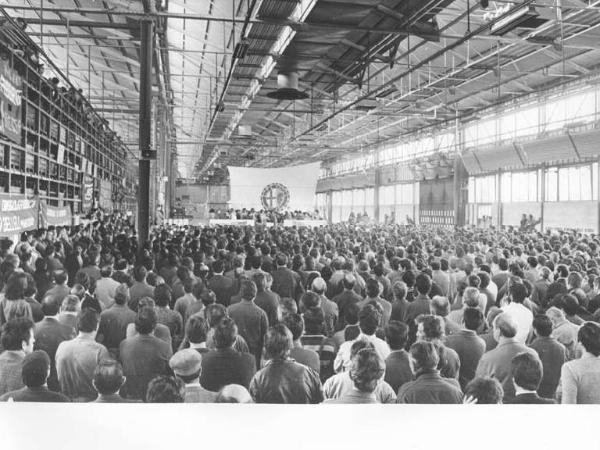 Fabbrica Alfa Romeo di Arese - Capannone - Interno - Celebrazione del 25 aprile - Panoramica sulla sala - Palco - Platea con i lavoratori - Striscioni - Logo dell'Alfa Romeo