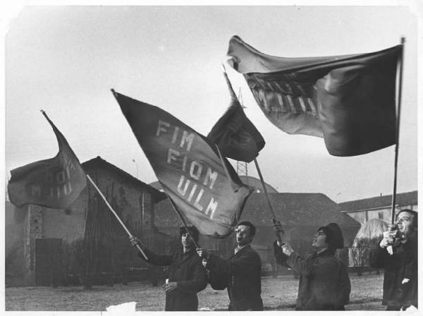 Sciopero dei lavoratori della Redaelli - Operai con tuta da lavoro sventolano bandiera Fim, Fiom, Uilm
