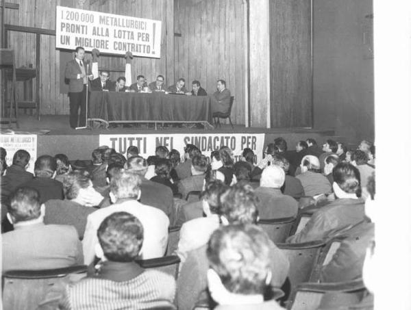 Piccolo Teatro - Interno - Assemblea dei lavoratori metalmeccanici per il rinnovo del contratto - Palco - Intervento di Annio Breschi - Tavolo della presidenza: tra gli oratori Pierluigi Perrotta e Pierre Carniti - Striscione - Ordine del giorno