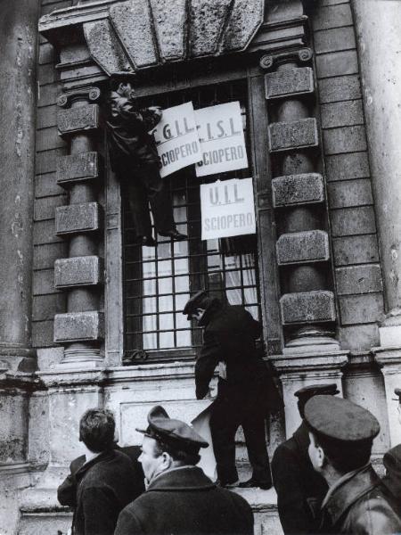 Milano - Sciopero tranvieri per una nuova politica dei trasporti - Manifestazione - Due lavoratori attaccano cartelli di Cgil, Cisl e Uil ad una finestra